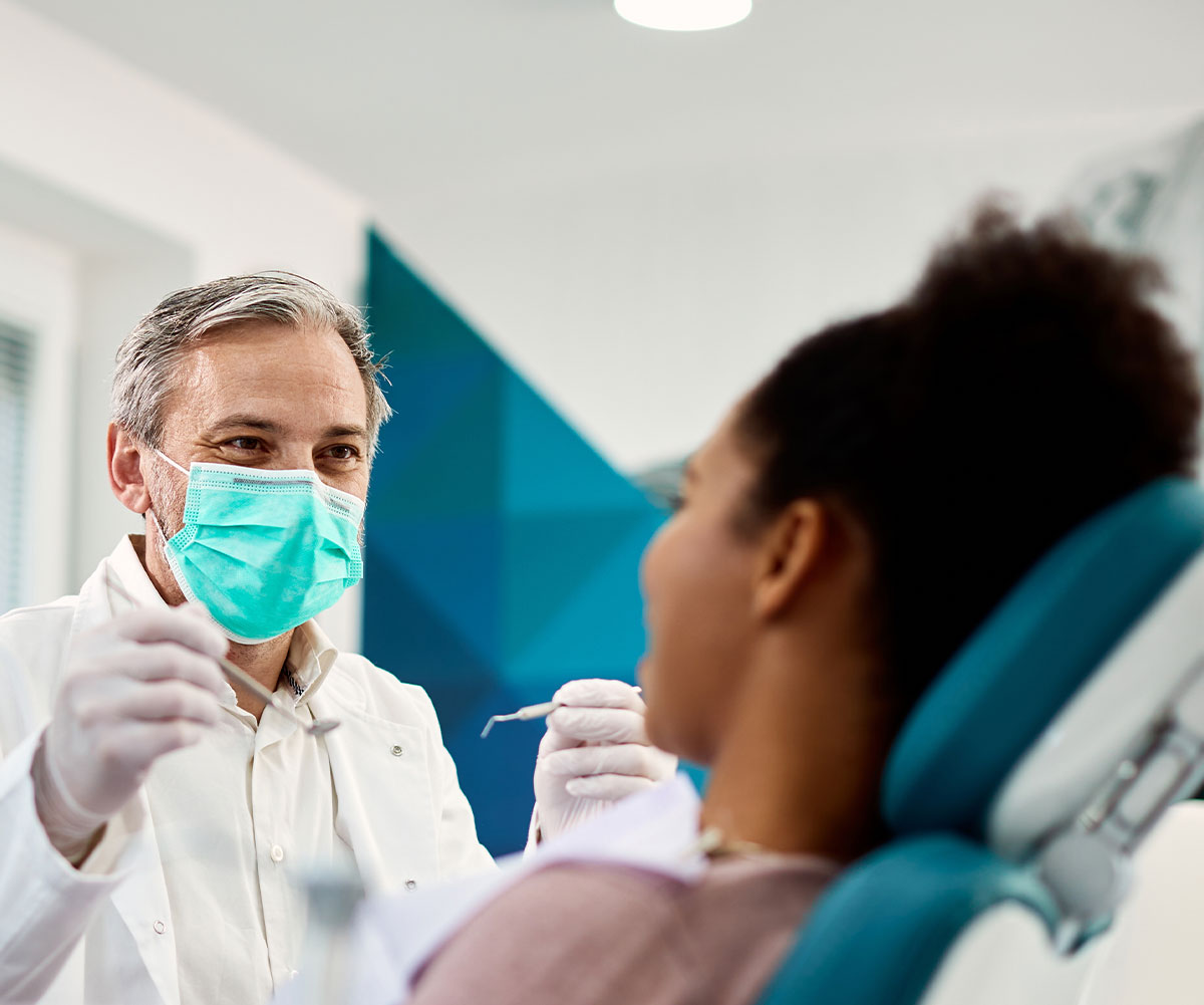 A dental professional in a mask, providing care to a patient seated in a dental chair.