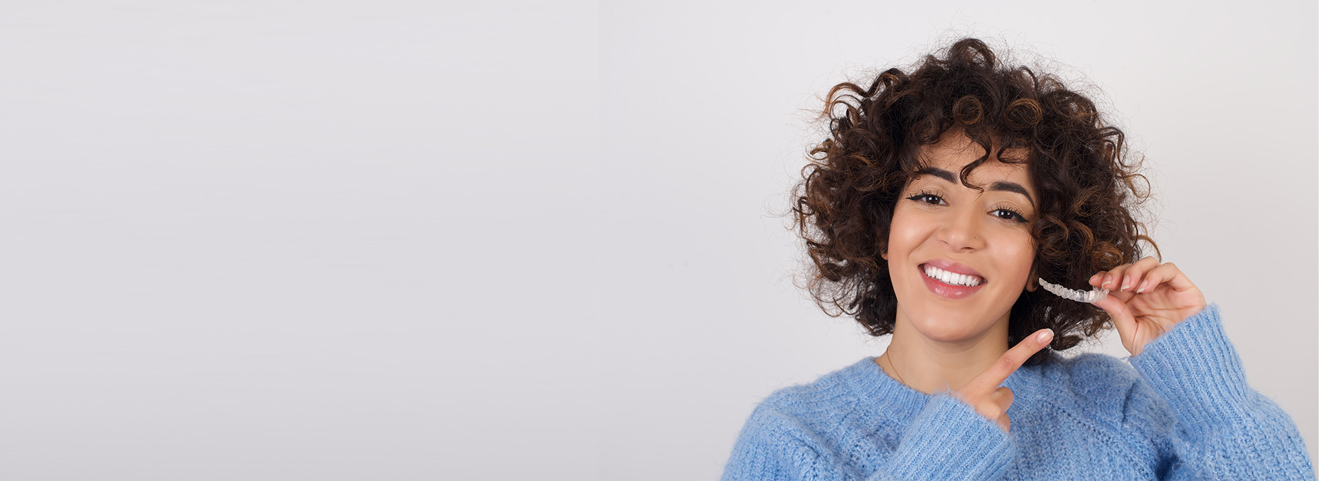 A woman with curly hair smiling at the camera, against a white background.