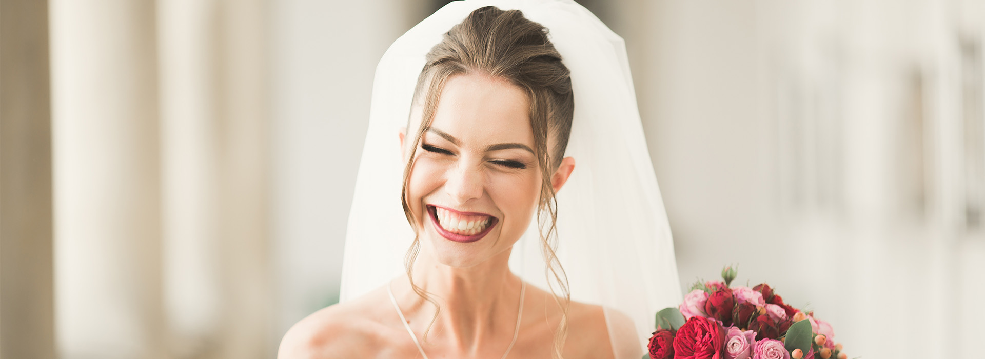 A bride wearing a white wedding dress, laughing and looking away from the camera.