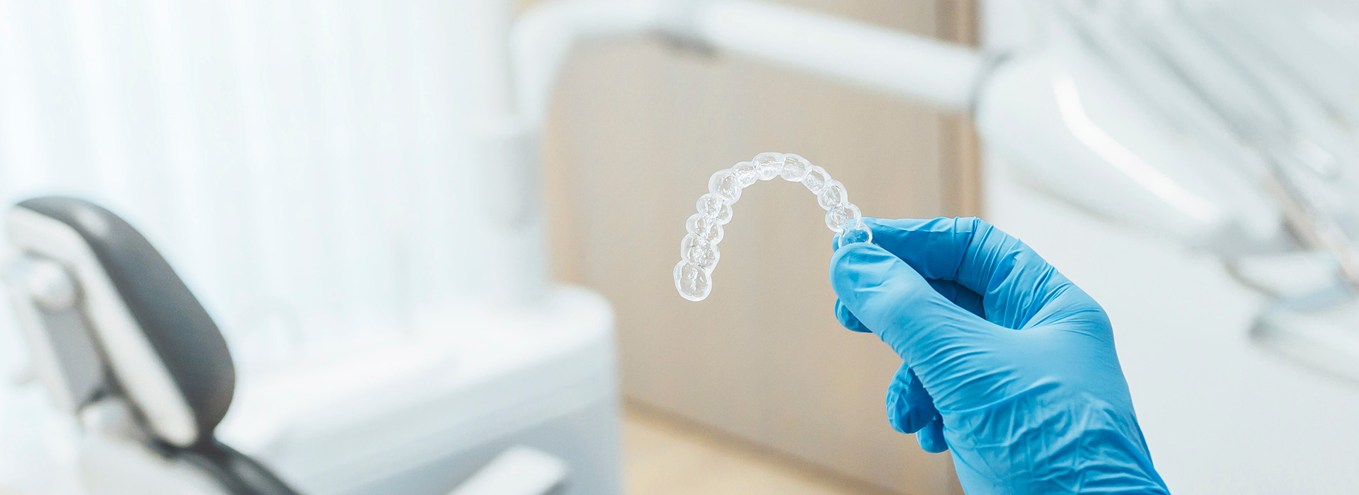 A close-up of a dental professional s hand holding a transparent impression tray over a dental chair, with a focus on the tray and the professional s glove.