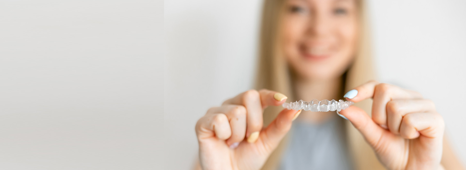 A smiling woman holding a ring with her left hand against a blurred background.