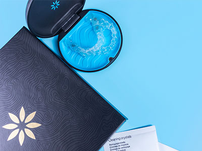 A blue toothbrush with a handle in a black case, placed next to a box of dental floss on a light blue background.