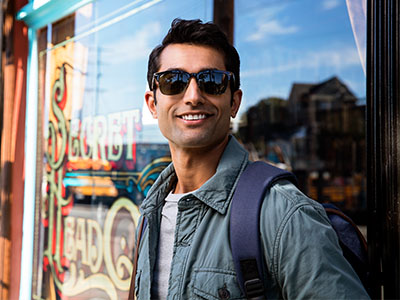 A man in sunglasses standing outside a storefront, smiling and looking towards the camera.