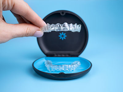 An image of a person s hand holding an open, black dental appliance case containing a clear dental aligner tray with several white plastic teeth.