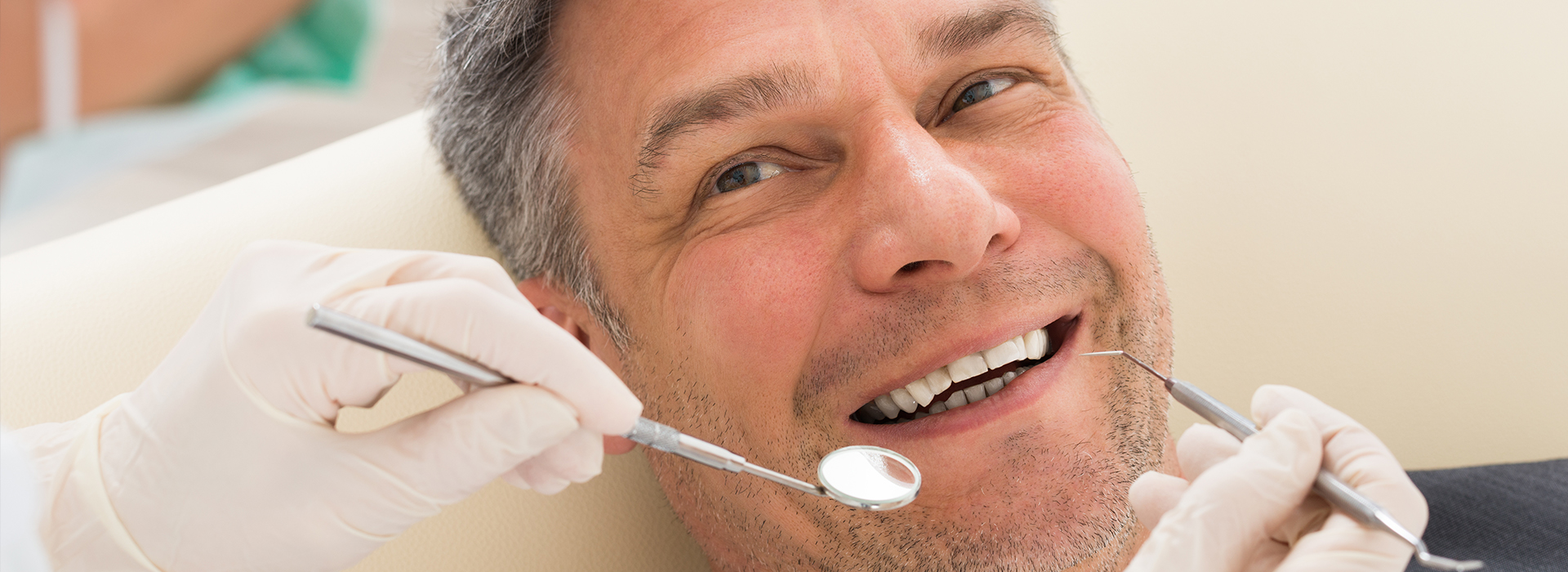 A man sitting in a dental chair, smiling broadly as he receives dental care from a professional.