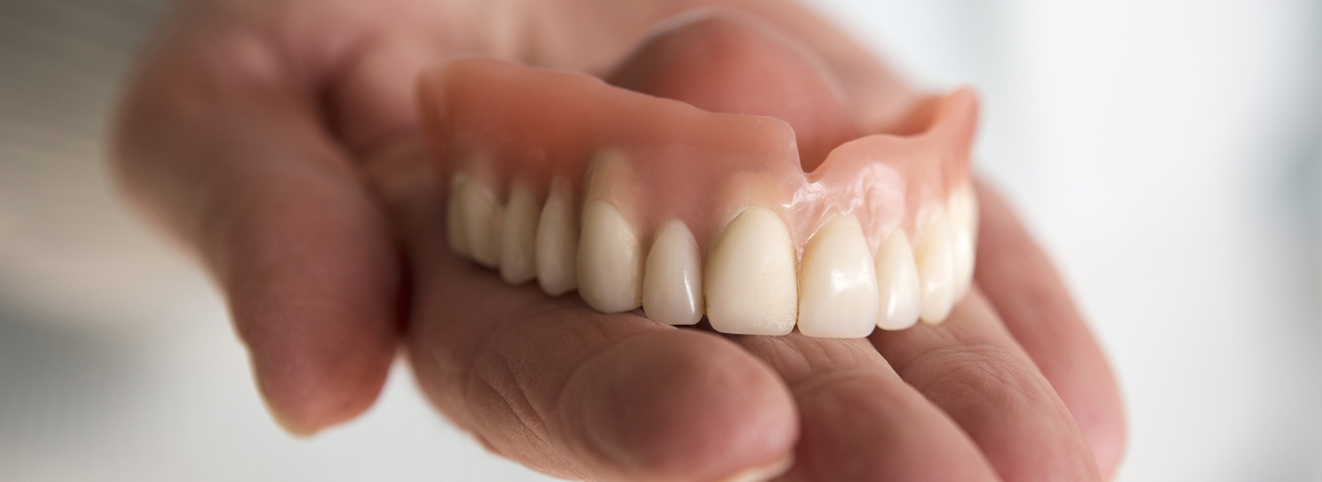 The image shows a person holding a set of dentures in their hand.