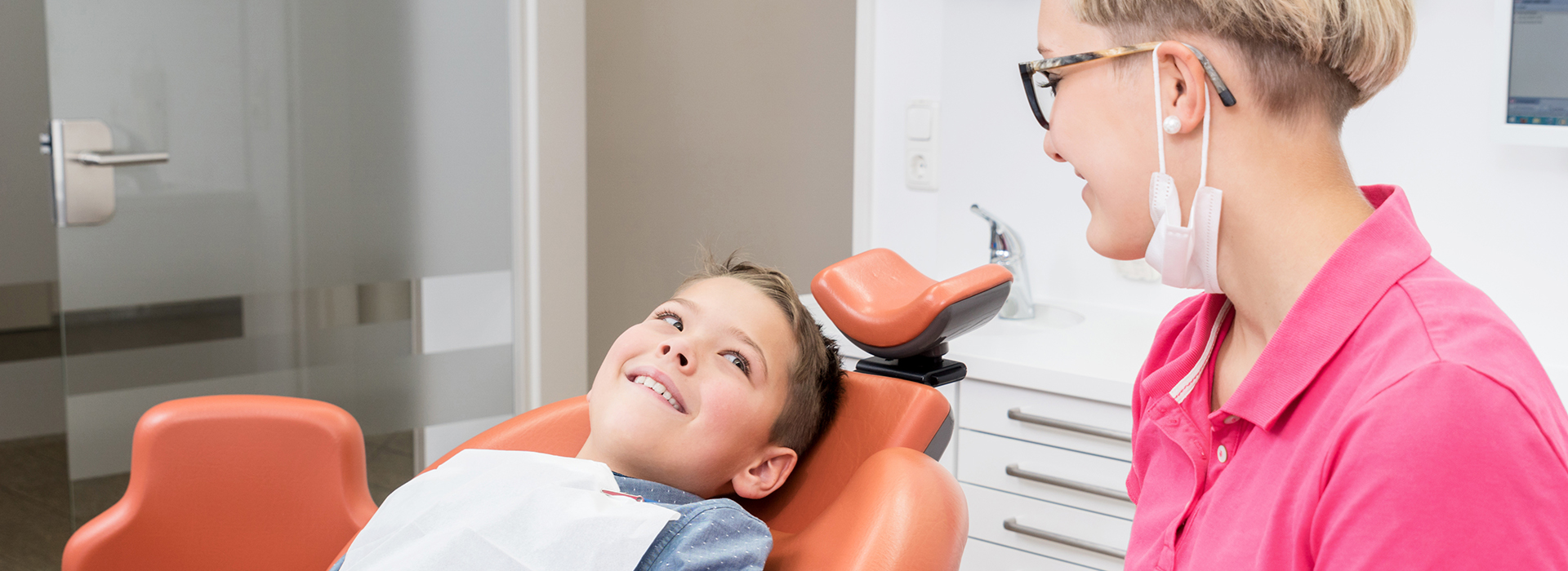 A young boy receiving dental care, seated in a dental chair with a dentist and dental hygienist assisting.