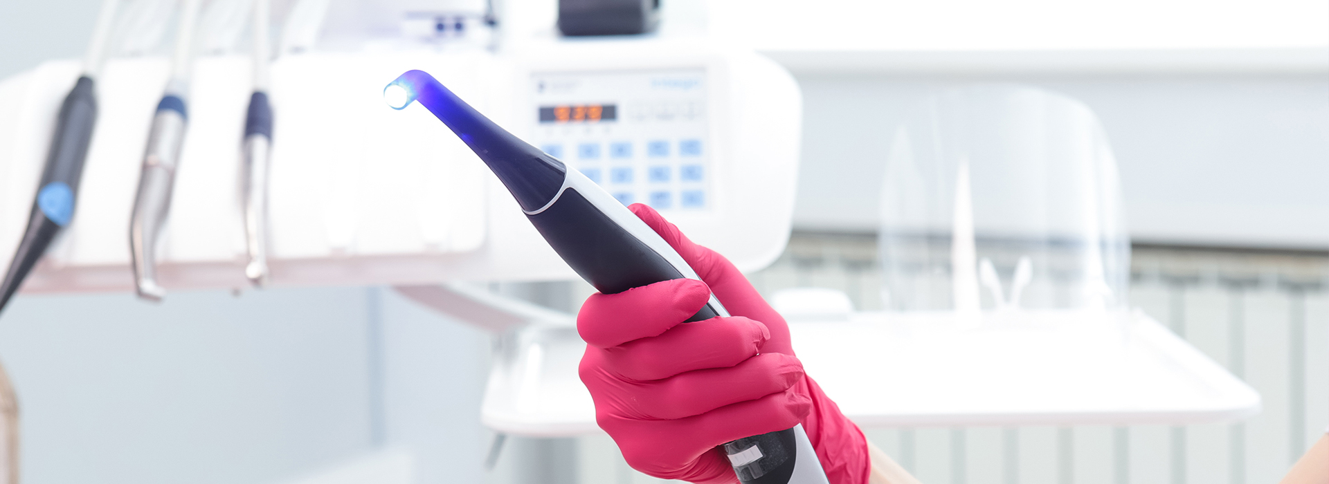 An individual in a medical or dental setting holding a blue device, likely related to dental care, while wearing protective gloves and a pink apron.