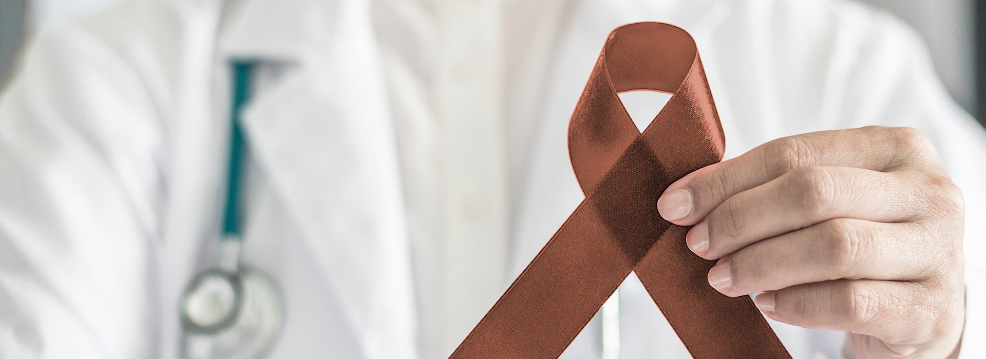 A medical professional holding a brown ribbon in front of their face, symbolizing awareness for a specific condition.