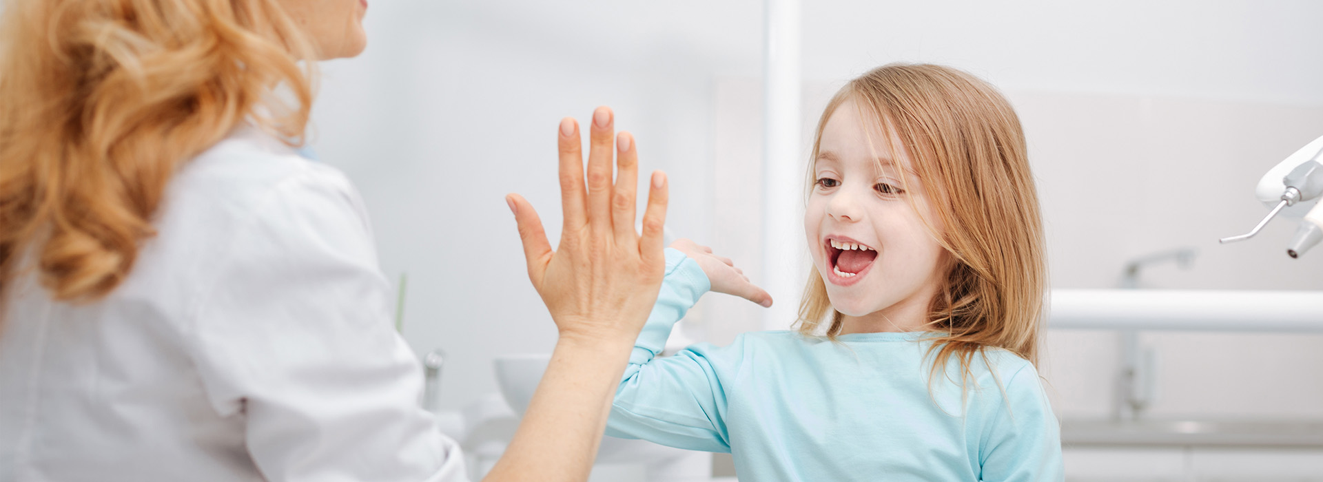 A woman and a young girl in a dental office, with the woman assisting the child.