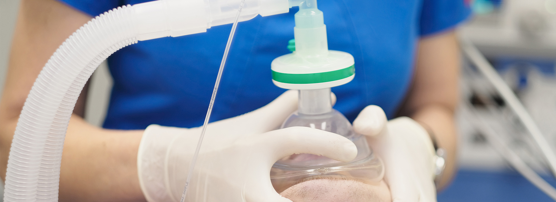 A person in a lab coat is handling a medical device with tubes and a green cap, possibly preparing it for use.