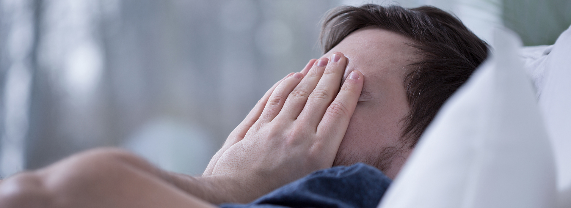 The image depicts a person lying in bed, covering their face with one hand, and appears to be resting or sleeping.