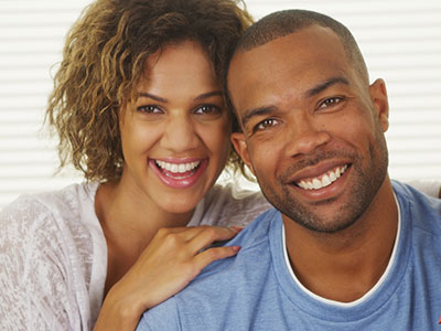 A man and a woman smiling at the camera, with the man wearing a blue t-shirt and the woman in a white blouse.