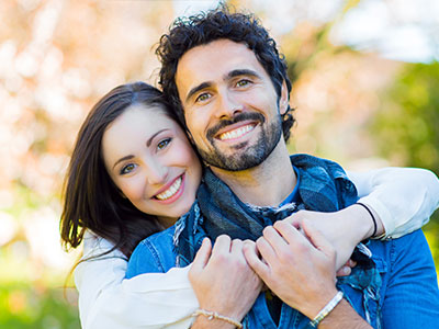 A man and a woman embracing warmly, smiling at the camera.