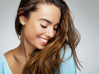 A smiling woman with long hair, wearing a blue top, against a light background.