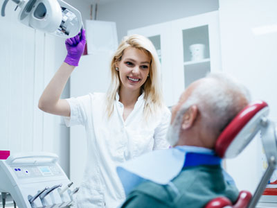 A dental professional in a white coat and purple gloves is assisting an elderly patient with a mechanical device, possibly for oral care or examination.