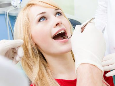 A woman receiving dental care, sitting in a dental chair with her mouth open and a dental practitioner attending to her.