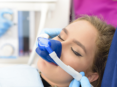 A person receiving medical treatment, with a blue oxygen mask attached to a machine and a healthcare professional assisting.